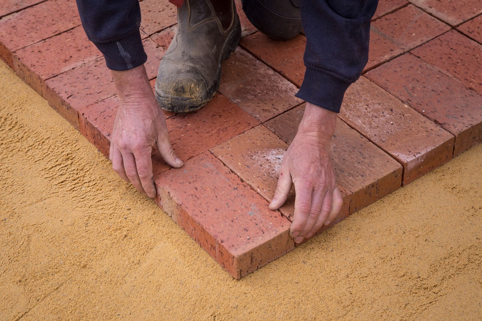 Brick pavers being hand-set on a compacted sand base