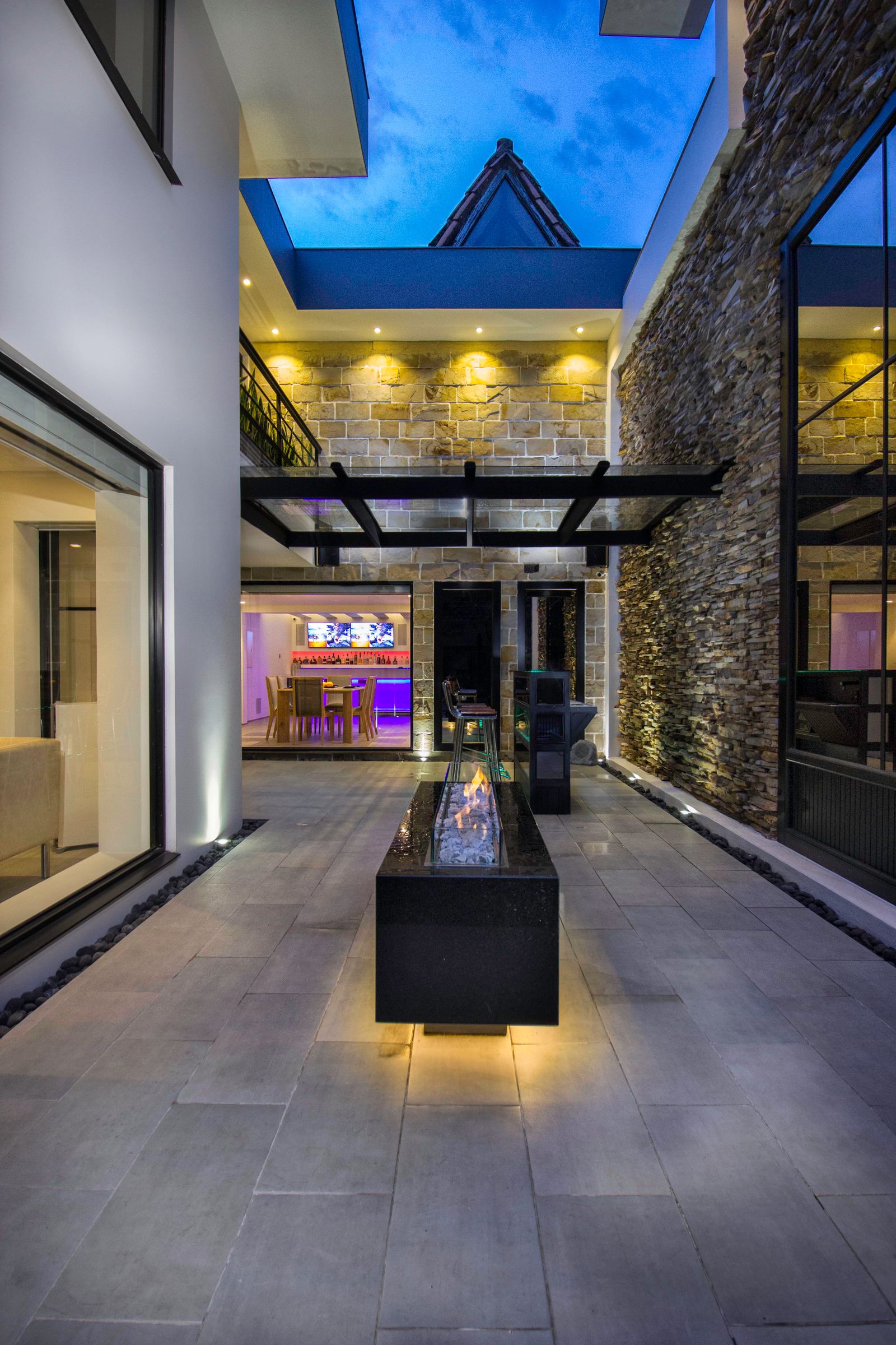 Large-format paver courtyard with a linear fire feature at dusk